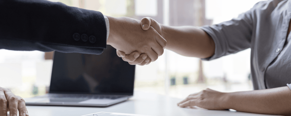 Zwei Personen geben sich im Büro die Hand – Symbol für Bewerbungsgespräch oder beruflichen Einstieg.