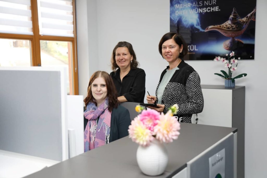 Drei Mitarbeiterinnen der Kalkül Steuerberatung im Büro. Rechts im Bild: Dorit Stephan, Geschäftsführerin. Freundliche Szene mit Blumen und Poster im Hintergrund.